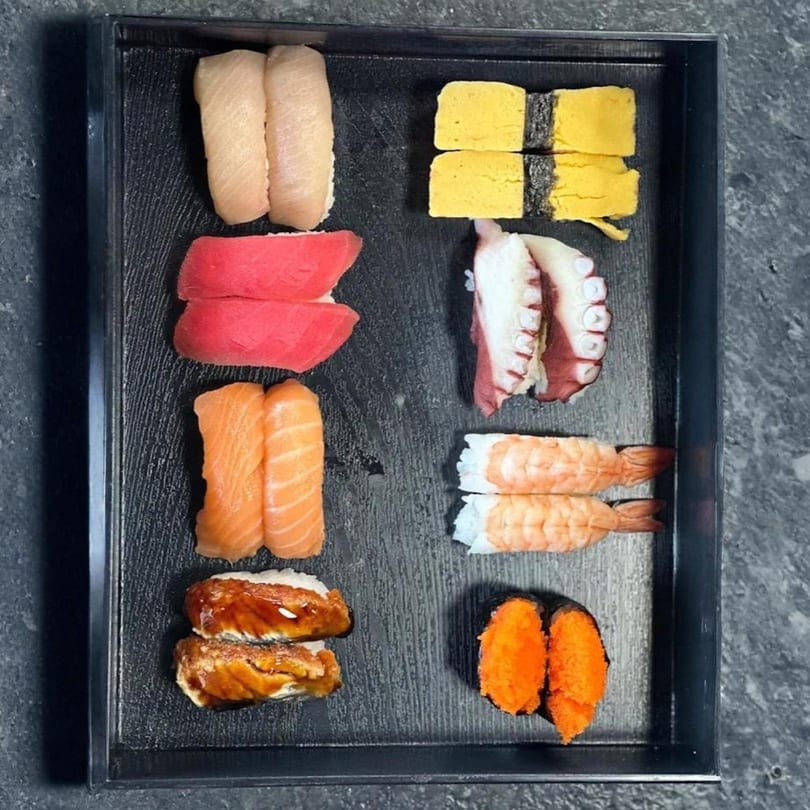 A black tray filled with various types of colorful sushi, including tuna, salmon, shrimp, and octopus.