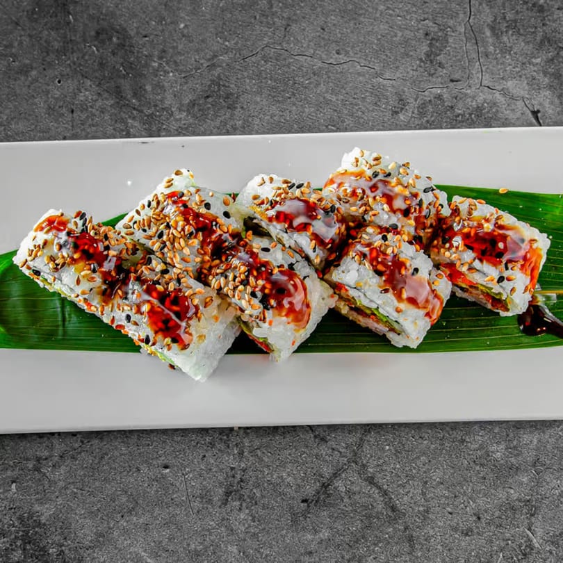 Sushi Fever's sushi rolls with sesame seeds and sauce, served on a banana leaf.