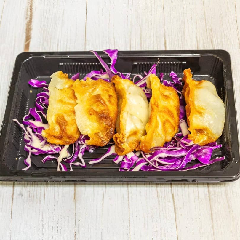 Five golden-brown fried gyoza dumplings rest on a bed of shredded purple cabbage in a black tray.