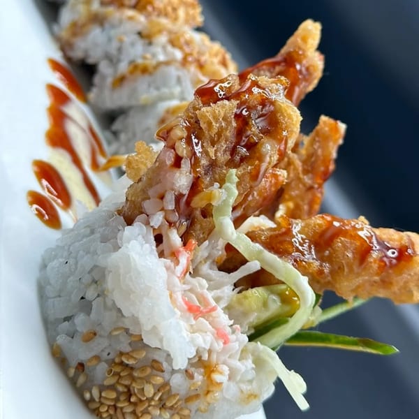 Sushi Fever's sushi roll with fried soft-shell crab, rice, sesame seeds, and drizzled sauces.