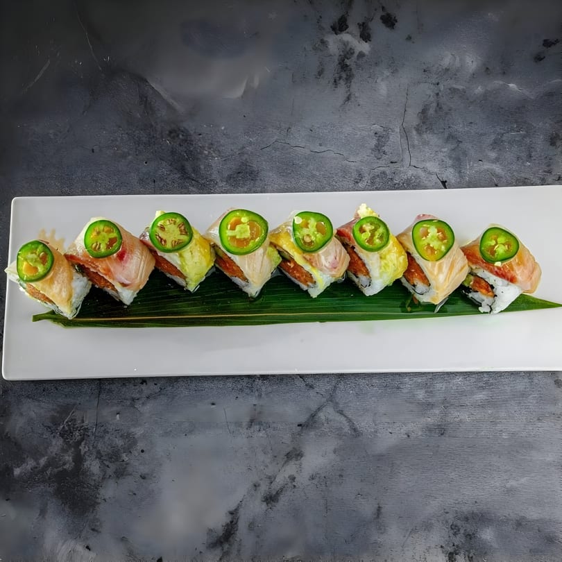 Eight pieces of sushi with fish, avocado, and jalapeño slices on a white rectangular plate.