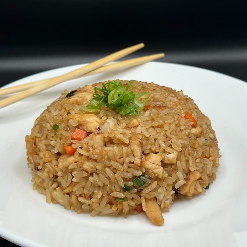 Chicken fried rice with carrots, green onions, and chopsticks on a white plate.